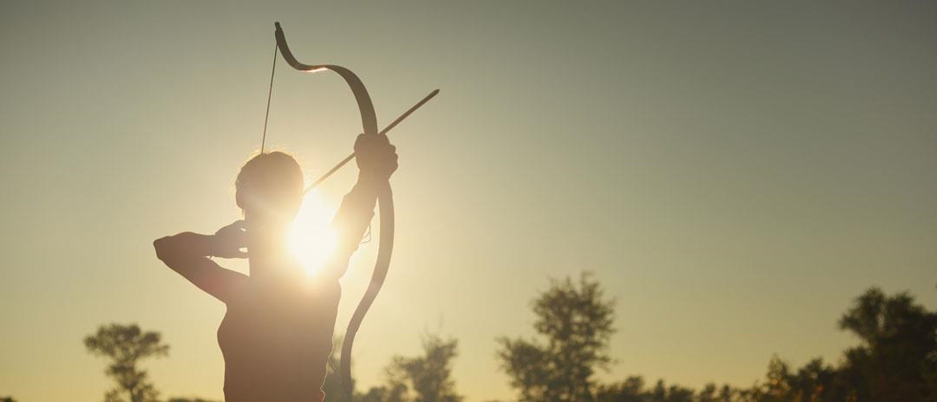Person beim Bogenschießen im Gegenlicht bei Sonnenuntergang.