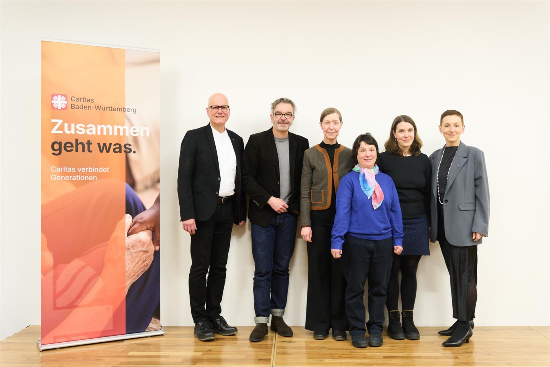 Fünf Personen stehen mit einer Urkunde vor einem Caritas Baden-Württemberg vor einem Banner.