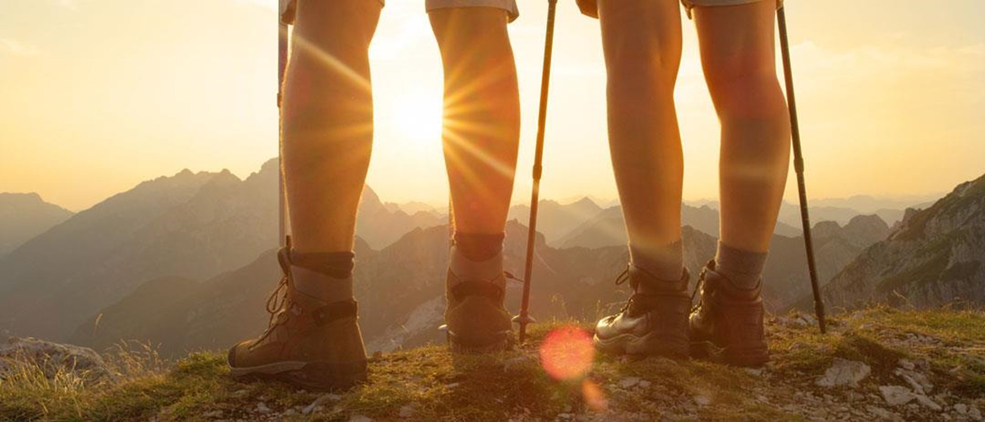 Wanderer mit Stöcken stehen bei Sonnenuntergang auf einem Berggipfel.