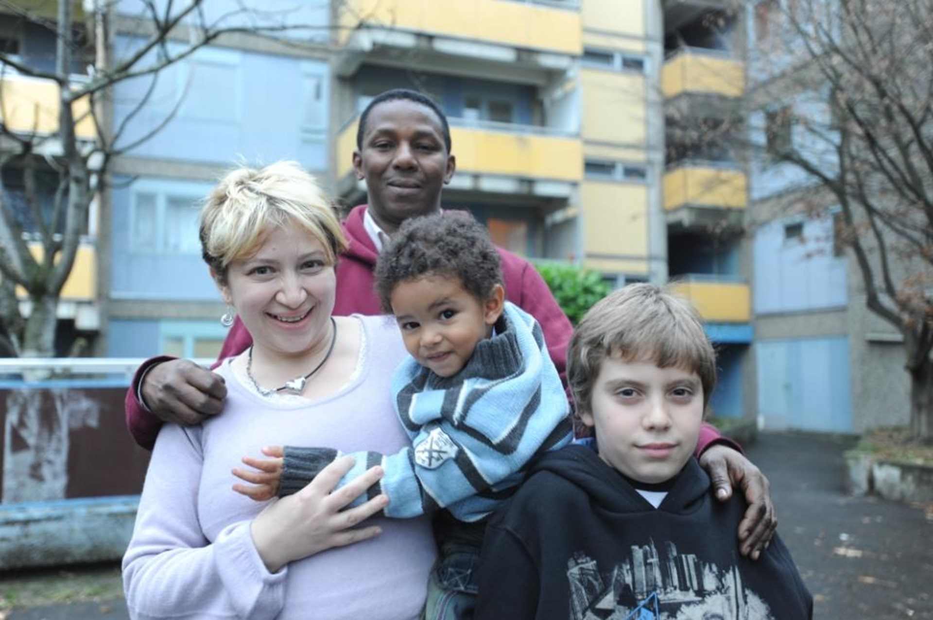 Ein vierköpfige Patchworkfamilie steht vor einem Mehrfamilienhaus